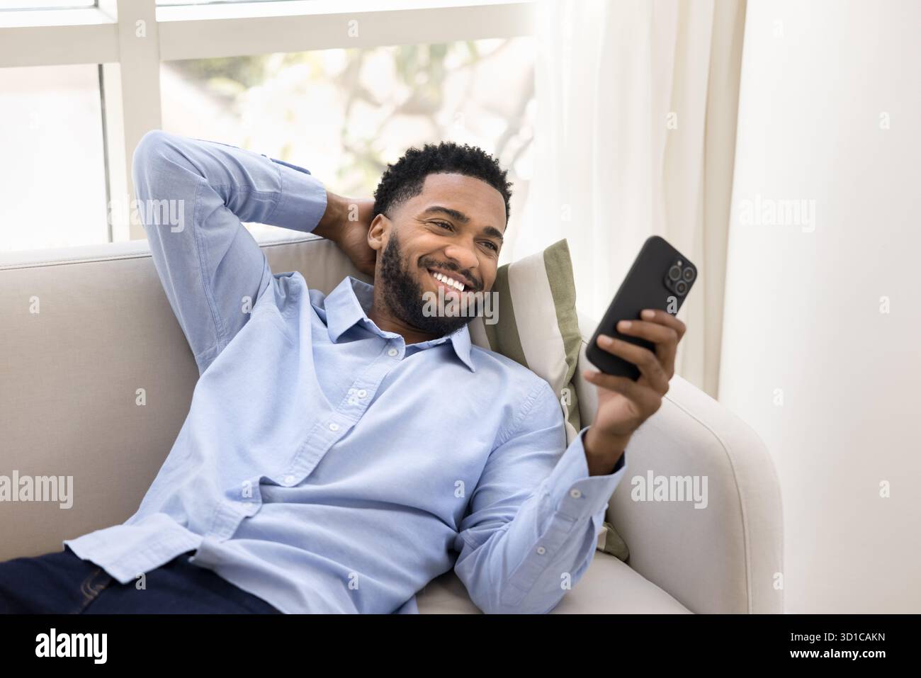 Young handsome smiling man lying on sofa with smartphone Stock Photo
