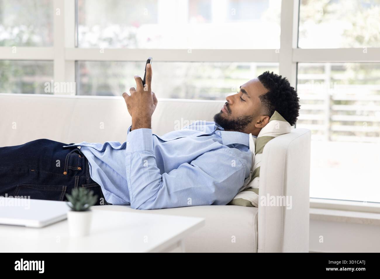 Young man lying on sofa while using his smartphone Stock Photo