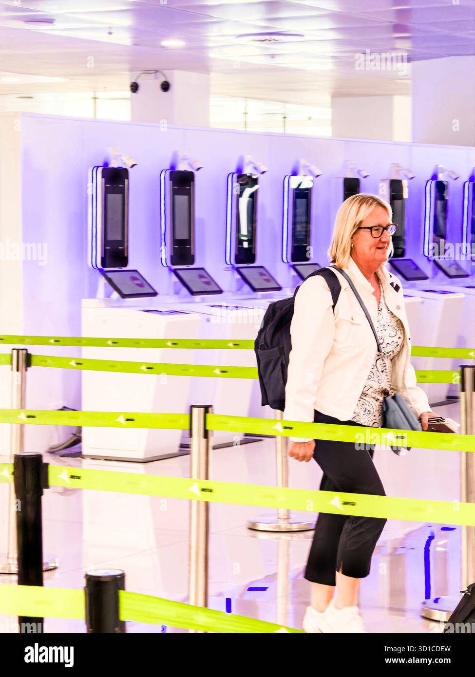 Woman with backpack walking through modern airport terminal near automated passport control kiosks - Smartphone Captured Stock Image Woman with backpack walking through modern airport terminal near automated passport control kiosks - Smartphone Captured Stock Image