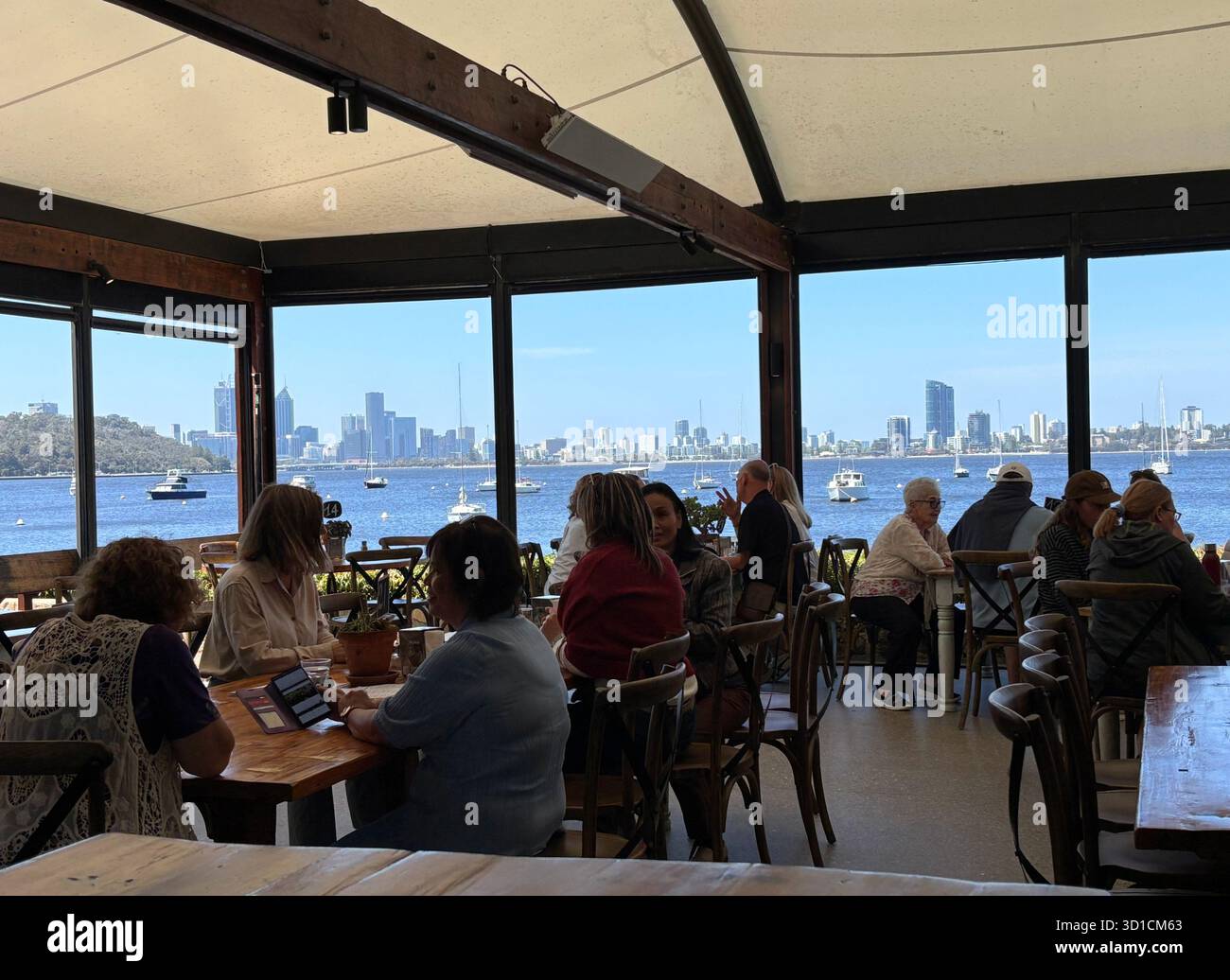 People eating and drinking on Swan River foreshore with Perth city skyline in the background, Bayside Kitchen, Crawley, Western Australia. No MR or PR - Smartphone Captured Stock Image