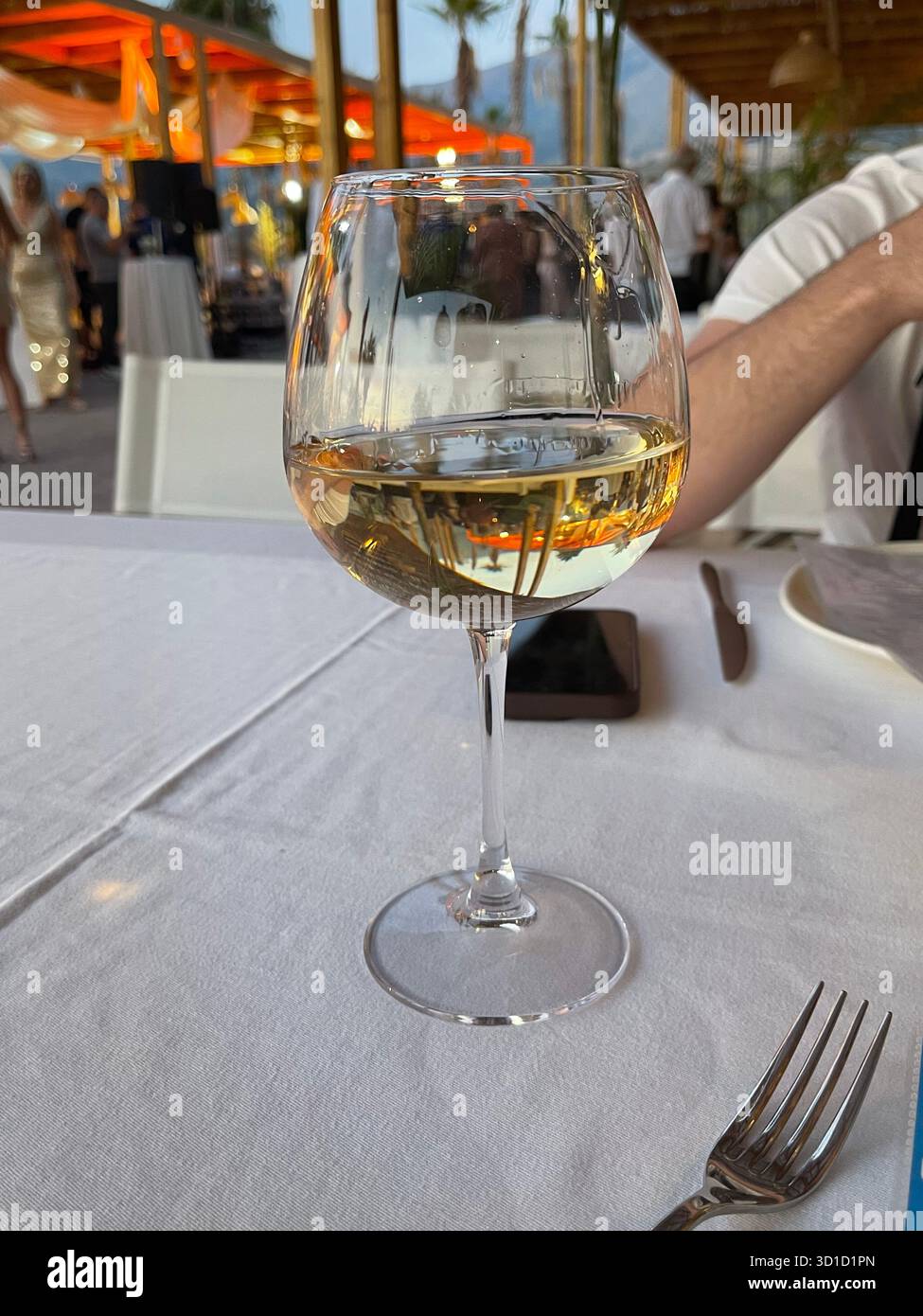 A glass of white wine on a table with a blurred restaurant background at sunset. - Smartphone Captured Stock Image