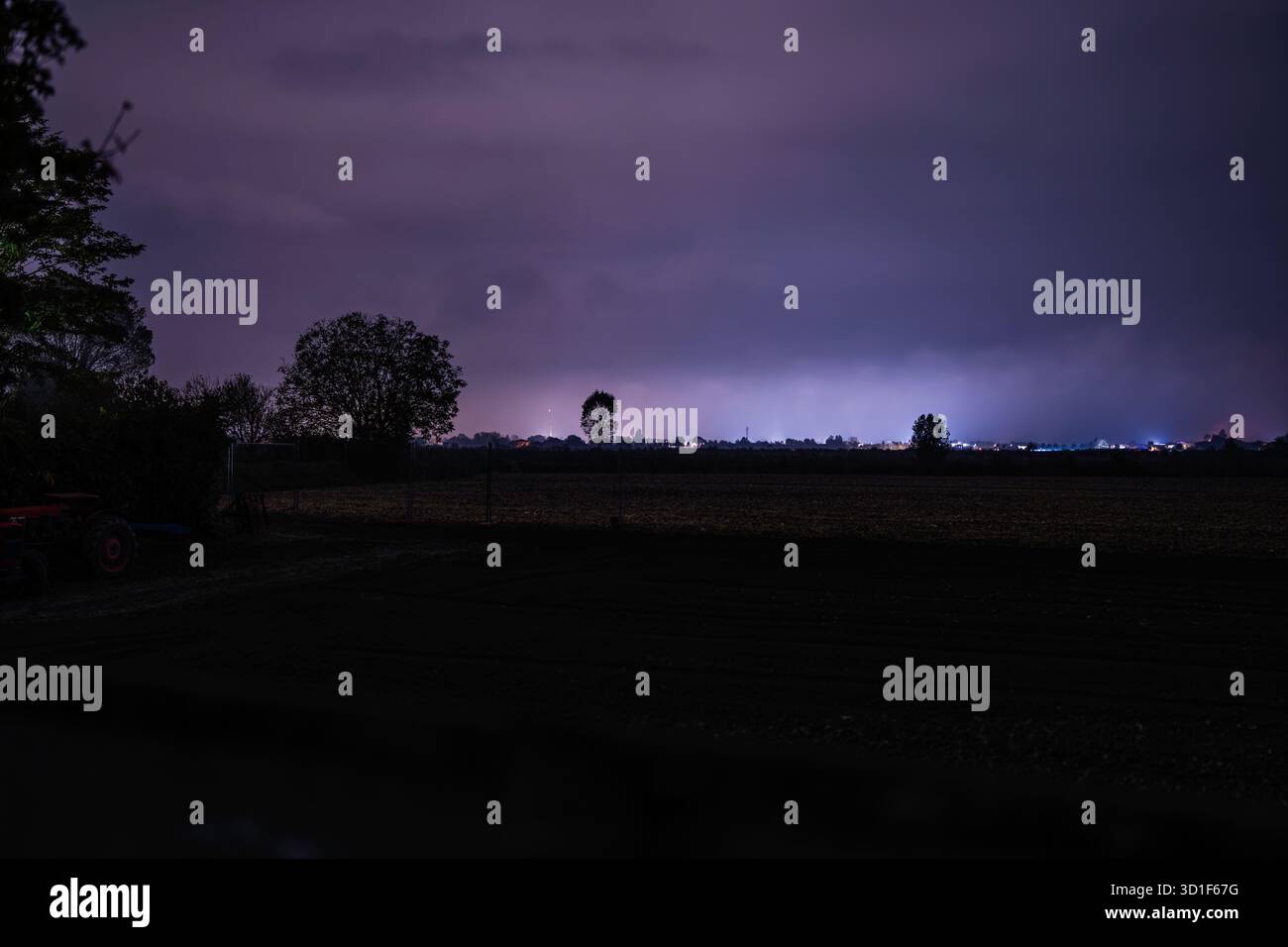 Night storm lightning forks across a deep purple sky over rural fields ...