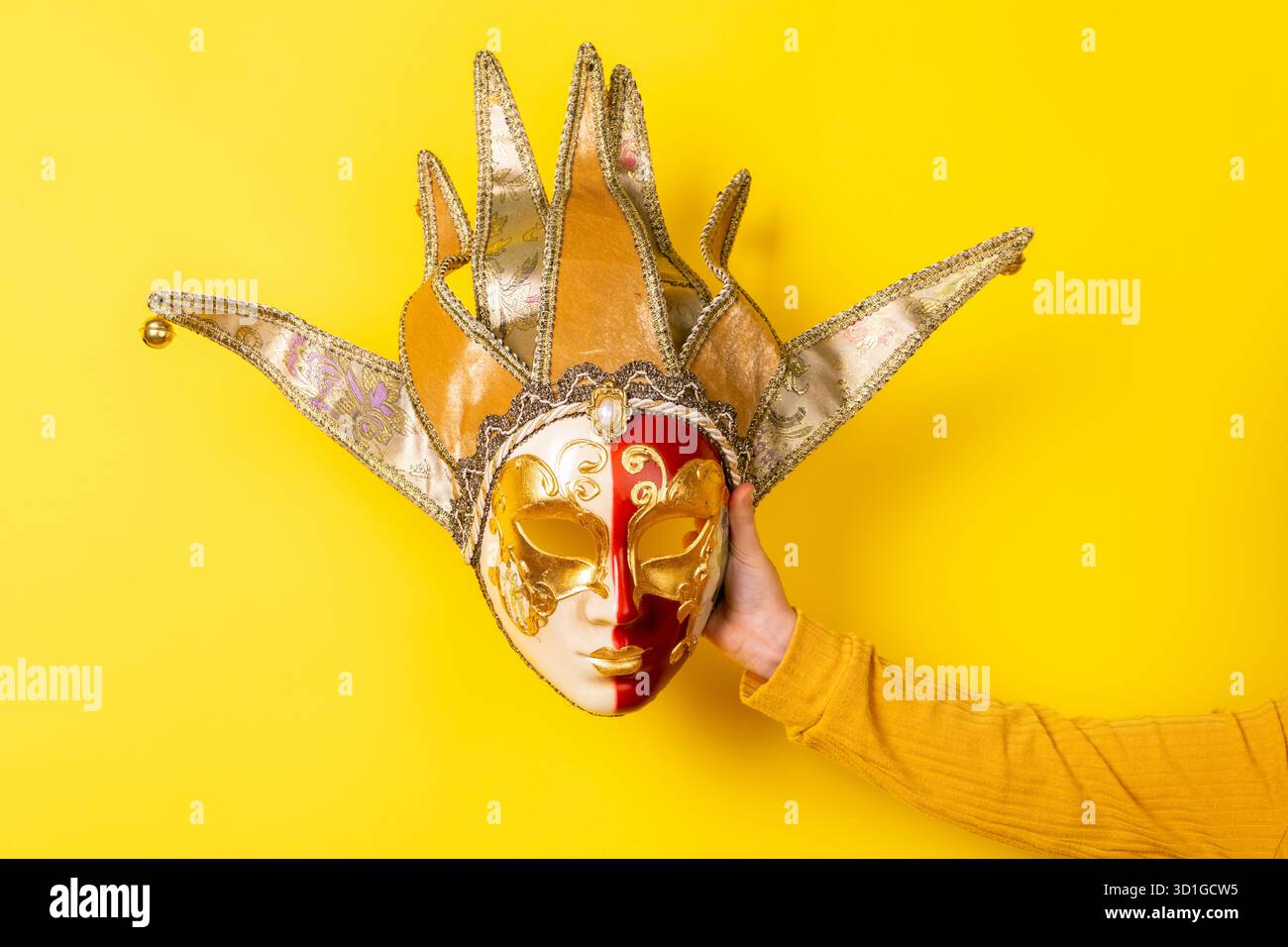 Hand holding ornate Venetian jester mask against vibrant yellow ...