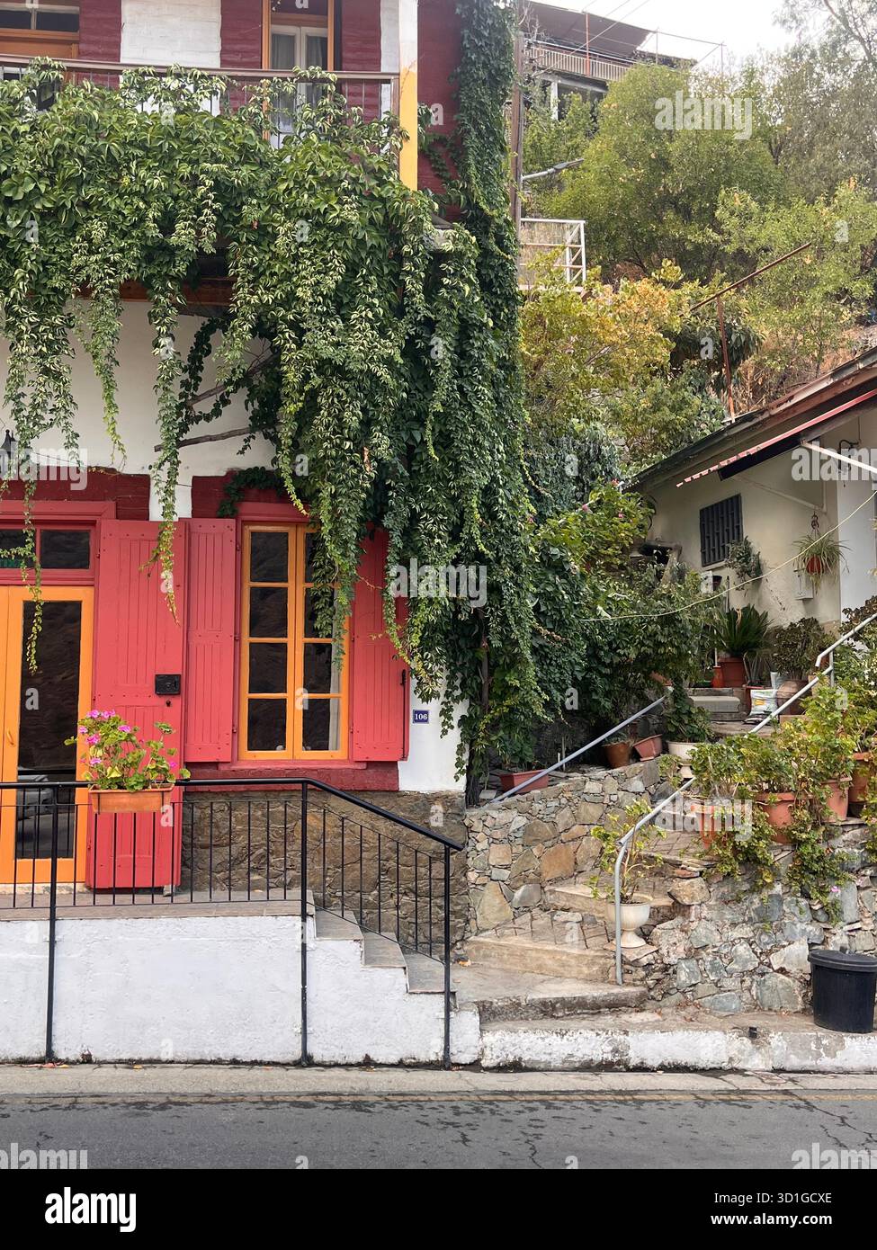 Cozy old greek white house with red elements covered in green plants - Smartphone Captured Stock Image