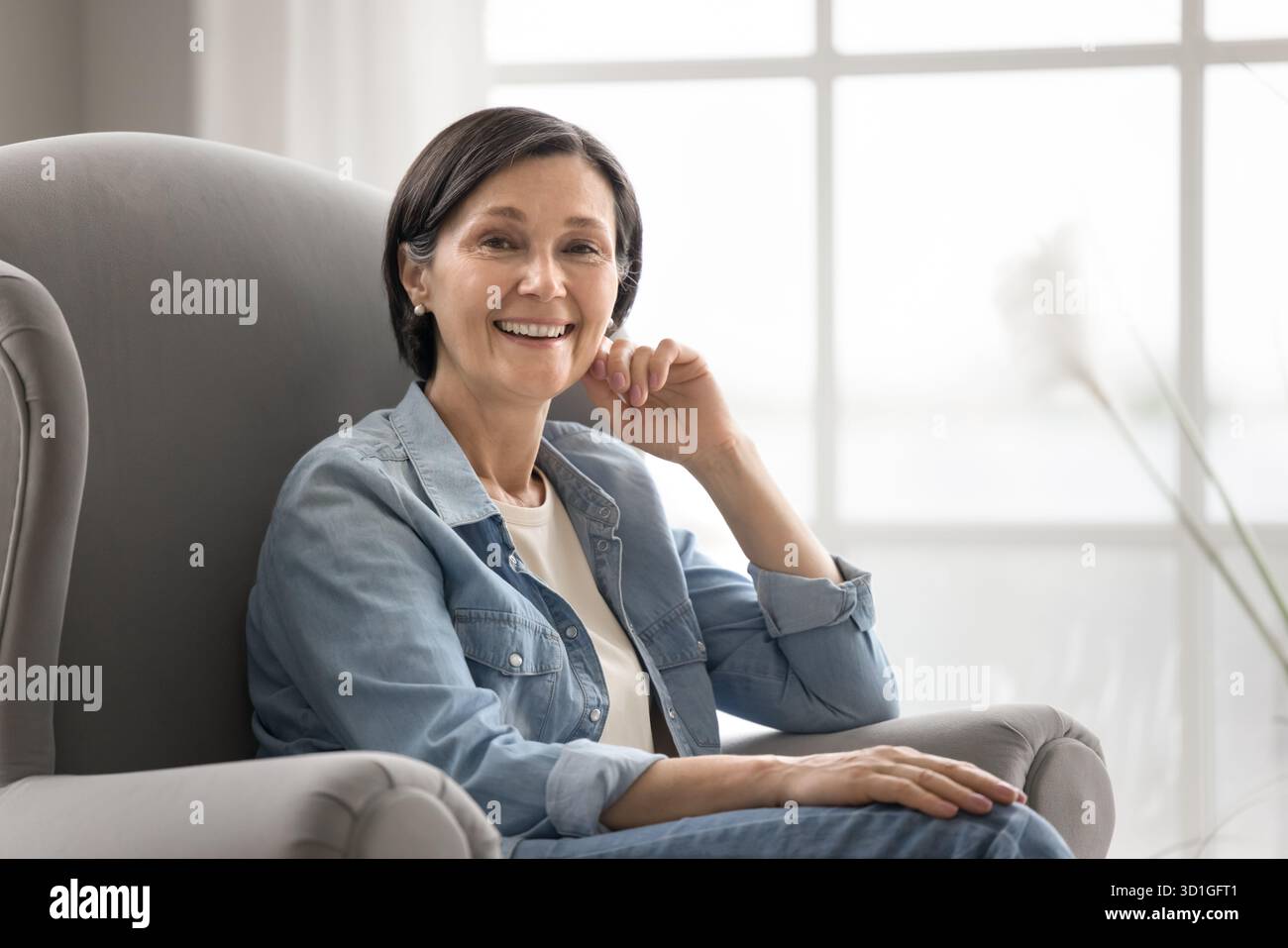 Portrait relaxed mature lady smiling at camera in comfy armchair Stock Photo
