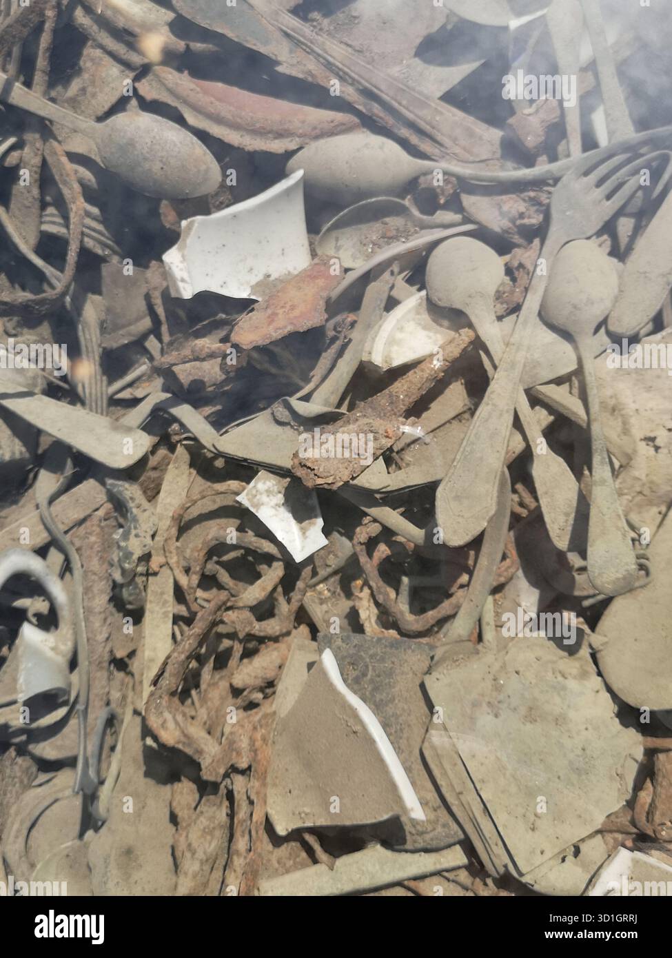 Scissors, trinkets, treasured items and utensils literally embedded in the ground at Auschwitz-Birkenau’s Kanada barracks—now preserved under glass. - Smartphone Captured Stock Image