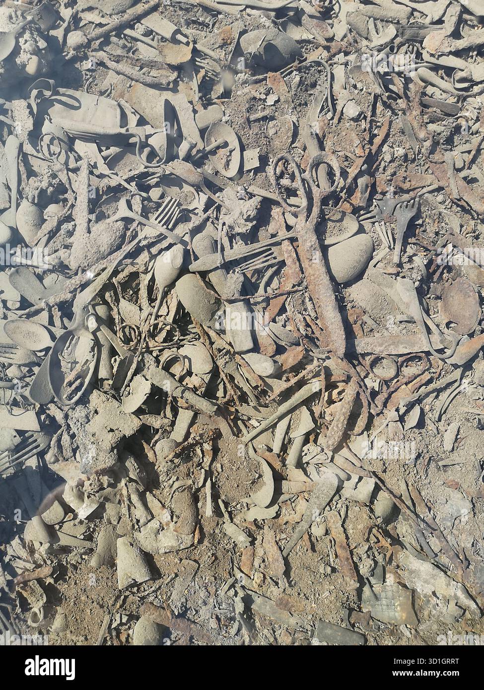 Scissors, trinkets, treasured items and utensils literally embedded in the ground at Auschwitz-Birkenau’s Kanada barracks—now preserved under glass. - Smartphone Captured Stock Image