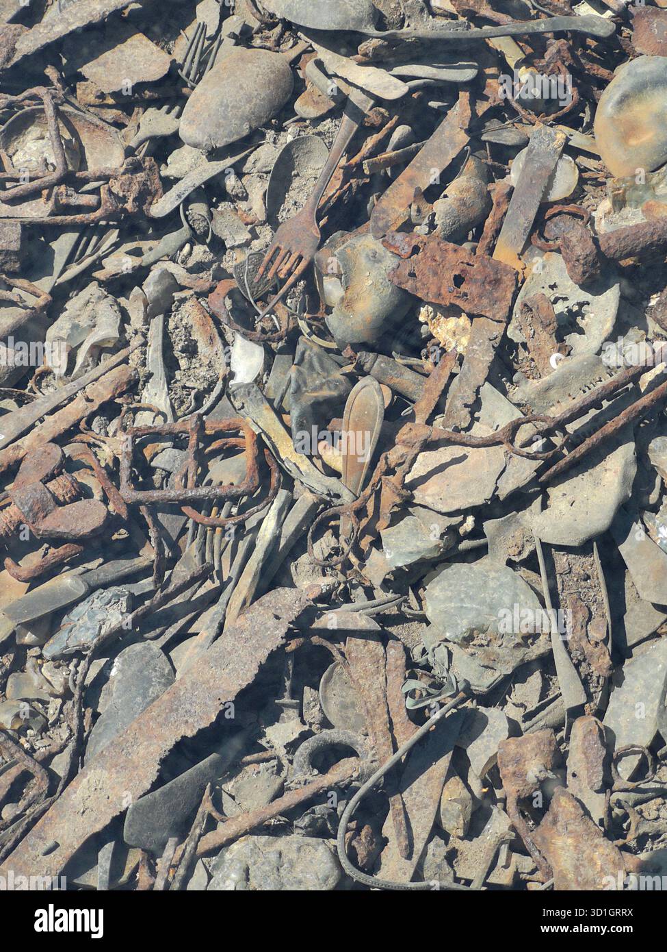Scissors, trinkets, treasured items and utensils literally embedded in the ground at Auschwitz-Birkenau’s Kanada barracks—now preserved under glass. - Smartphone Captured Stock Image