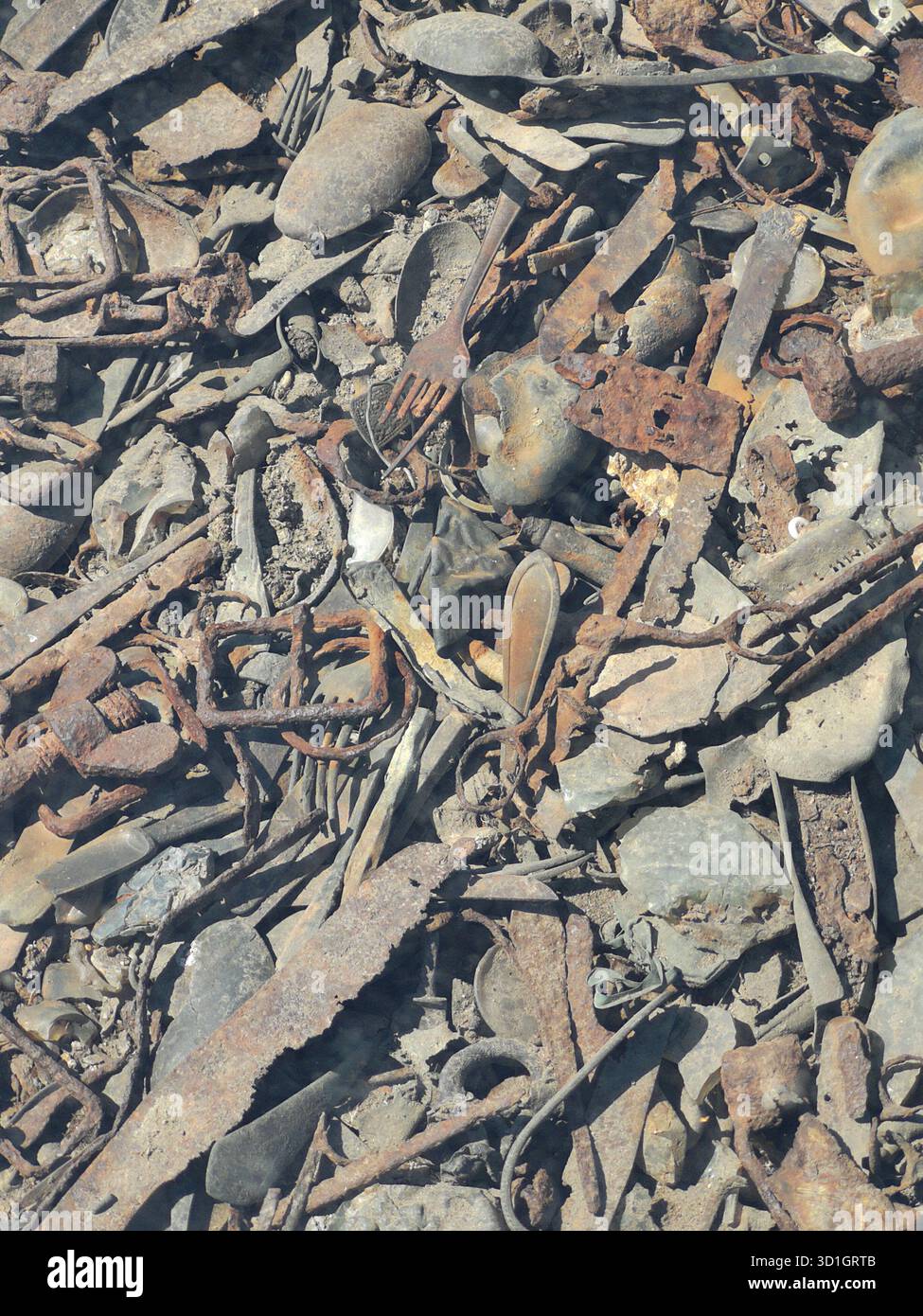 Scissors, trinkets, treasured items and utensils literally embedded in the ground at Auschwitz-Birkenau’s Kanada barracks—now preserved under glass. - Smartphone Captured Stock Image
