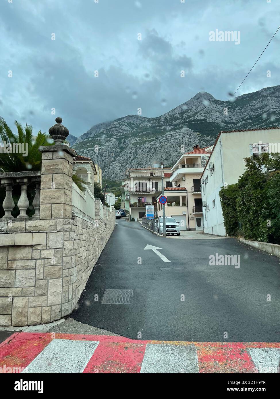 View down a residential street in a Croatian coastal town, characterized by light-colored apartments and a stone wall - Smartphone Captured Stock Image
