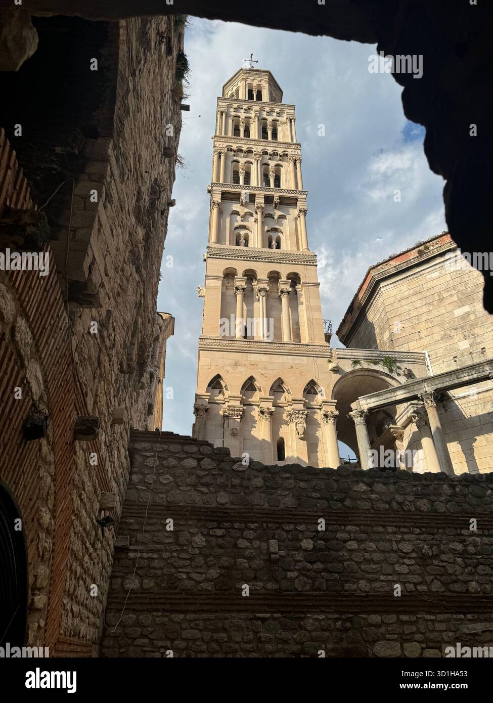 The iconic Bell Tower of the Cathedral of Saint Domnius in Split, Croatia, viewed through a narrow opening formed by the ancient stone walls - Smartphone Captured Stock Image