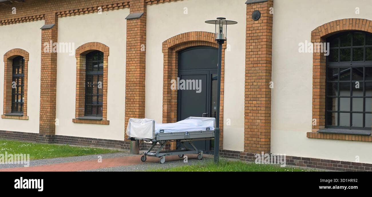 Belin, Germany - May 30, 2025: Hospital bed on wheels is positioned outside a building with a brick wall backdrop. Hospital - Smartphone Captured Stock Image