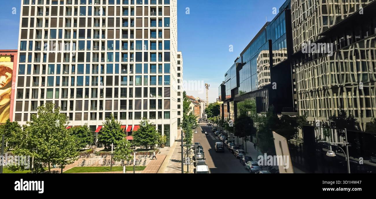 Berlin, Germany - May 13, 2025: Modern buildings line the street with greenery and clear blue sky creating a vibrant urban atmosphere. - Smartphone Captured Stock Image