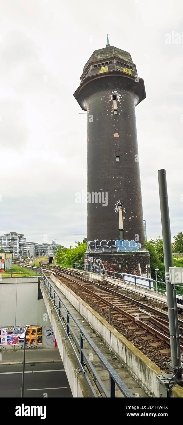 Belin, Germany - May 19, 2025: Historic black water tower stands next to railway tracks in urban environment. - Smartphone Captured Stock Image