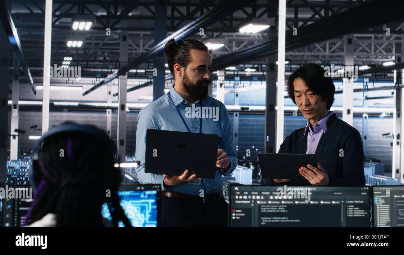 Data center manager supervising work done by programmers working on neural network software. Server hub supervisor overseeing IT staff members implementing deep learning tech, camera A Stock Photo