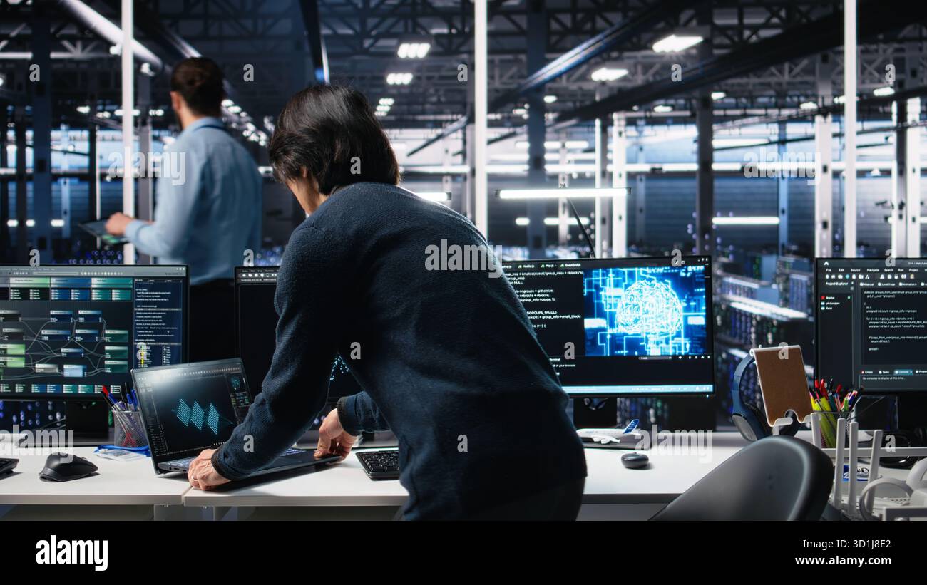 Technician arriving in data center office, coding with generative AI assistance. IT expert sitting at desk, starting work on artificial intelligence large language model solving tasks, camera A Stock Photo
