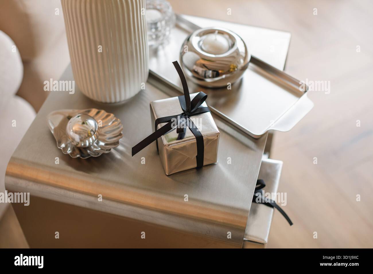 Overhead view of a wrapped Christmas gift on a coffee tablet assorted silver accessories and candles Stock Photo
