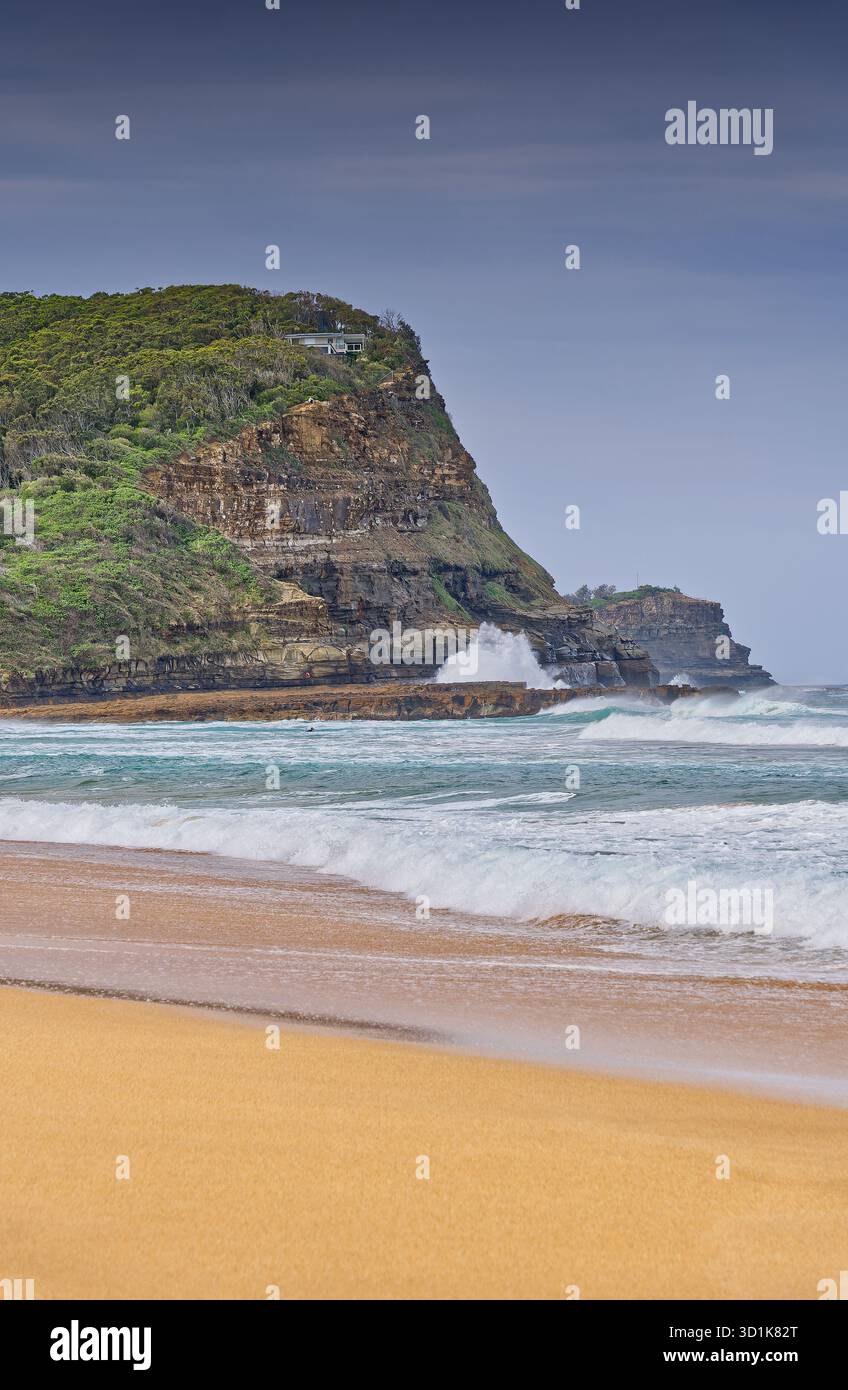 Sandy beach and rocky headland on overcast day with waves and surf at North Avoca beach, New South Wales, Australia Stock Photo