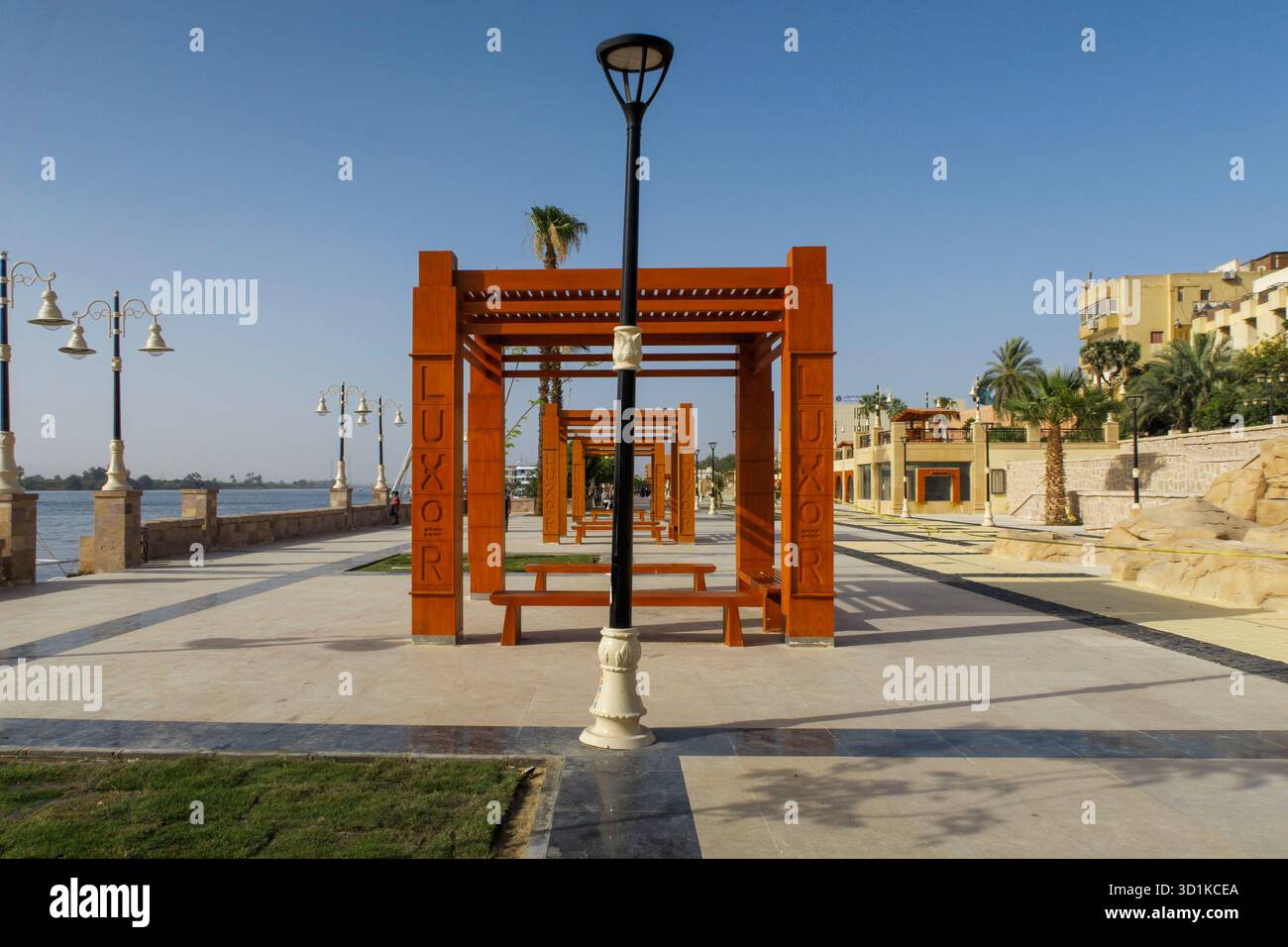 Sunny day along a modern riverside promenade with red pergolas and palm trees in Luxor Egypt showcasing urban development near the Nile Stock Photo
