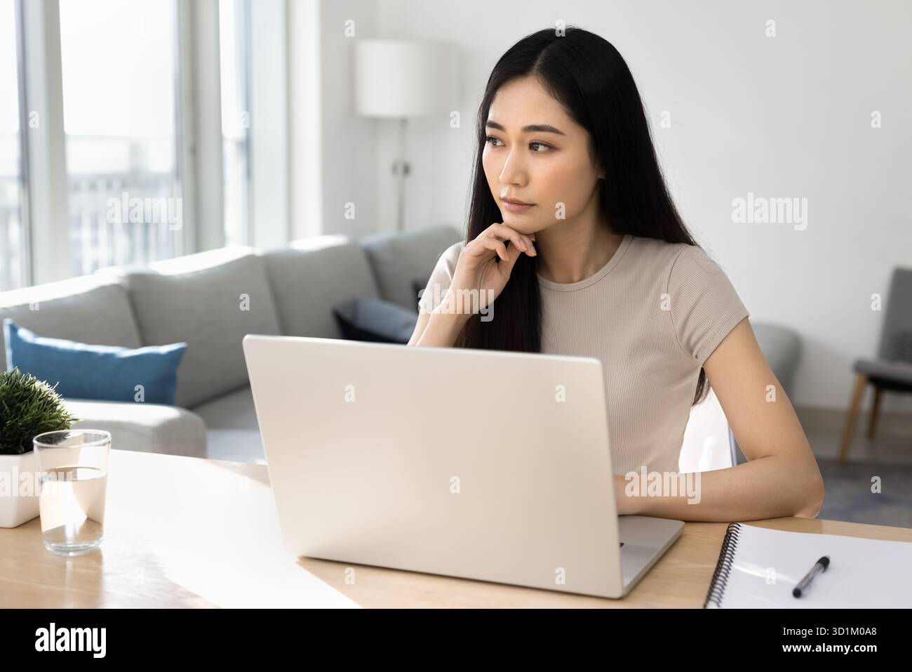 Thoughtful woman working on laptop at home Stock Photo
