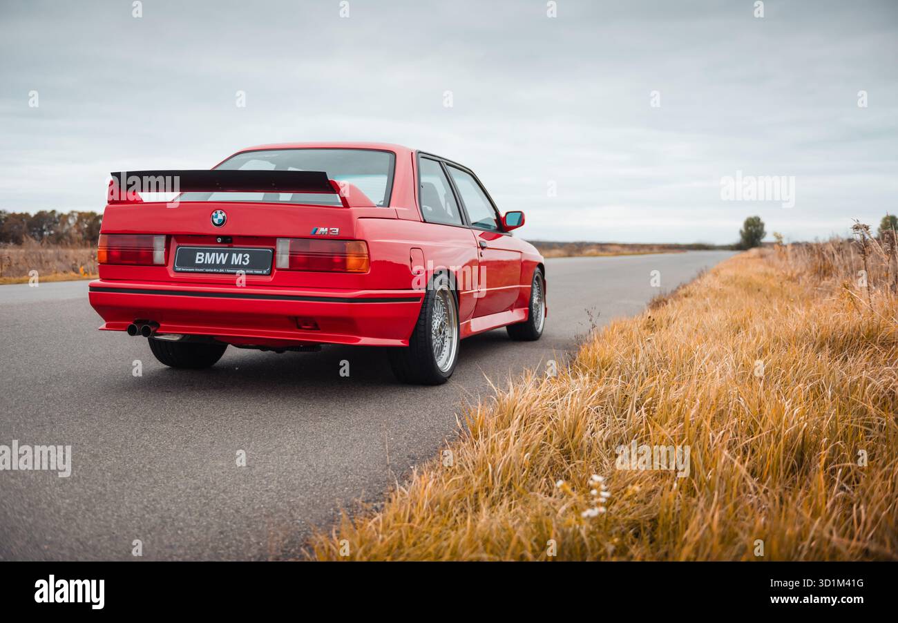Red BMW coupe on a rural road on autumn day. Three quarter rear view of ...