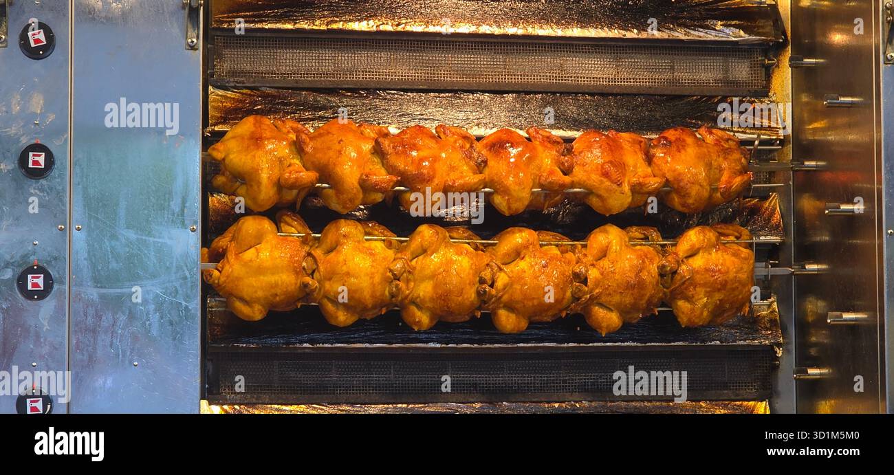 Roasted chickens are cooking on a rotisserie in a commercial kitchen, showcasing golden-brown skin and a busy culinary atmosphere. - Smartphone Captured Stock Image