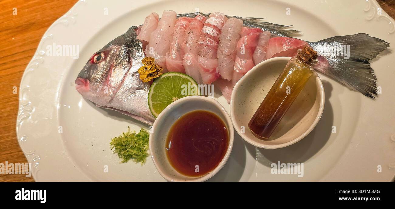 Freshly prepared fish is elegantly presented on a white plate with garnishes and dipping sauces, showcasing culinary artistry and flavor. - Smartphone Captured Stock Image