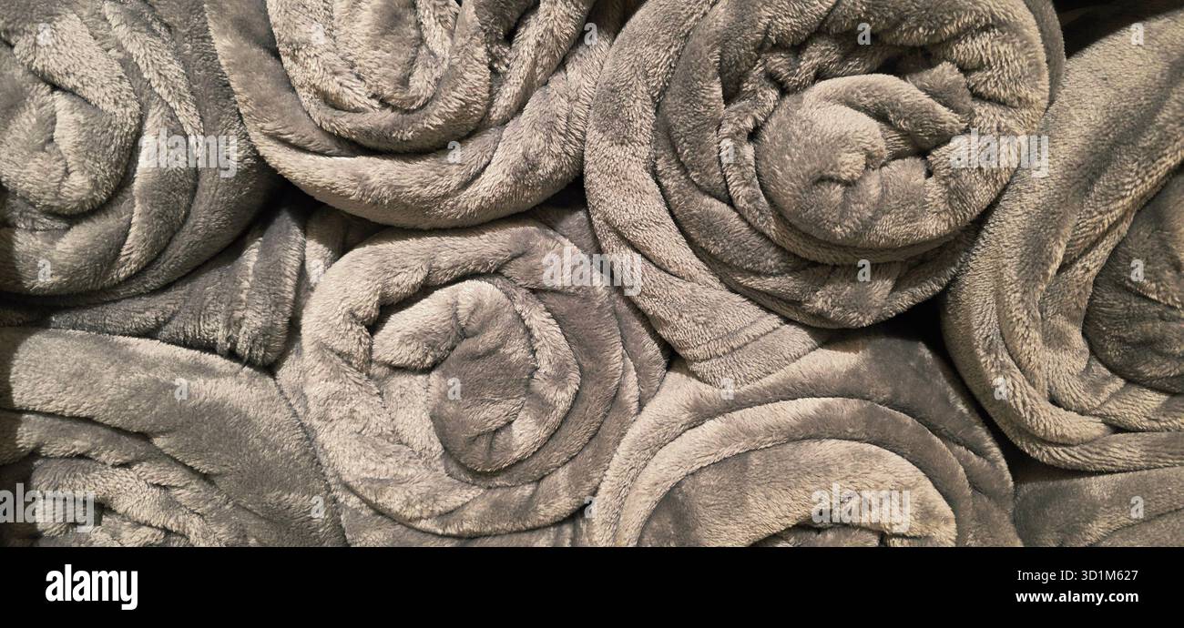 Soft gray blankets are rolled and stacked neatly, creating a cozy atmosphere perfect for home decor and comfort in any living space. - Smartphone Captured Stock Image