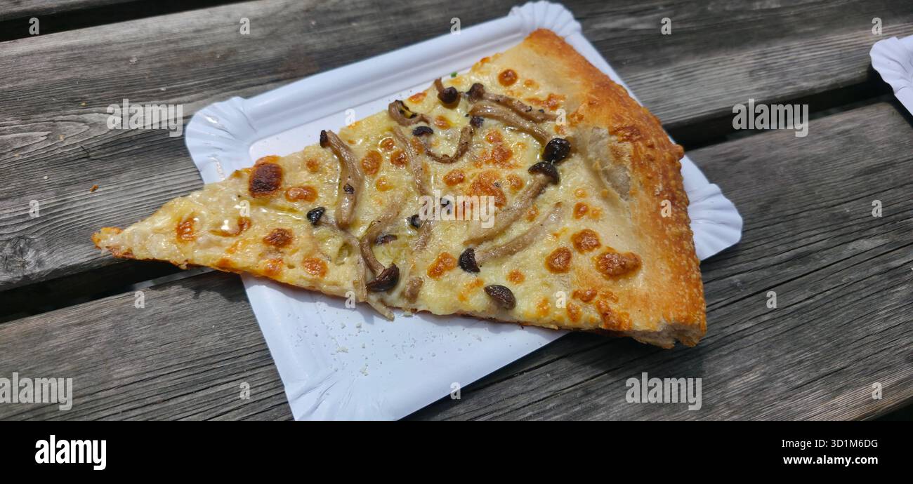 Gourmet pizza slice topped with mushrooms, placed on a white paper plate, resting on a rustic wooden table, showcasing appetizing textures and colors. - Smartphone Captured Stock Image