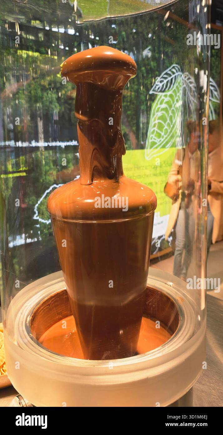 Chocolate fountain features rich, flowing chocolate in a clear display, surrounded by lush greenery and inviting atmosphere for dessert lovers. - Smartphone Captured Stock Image