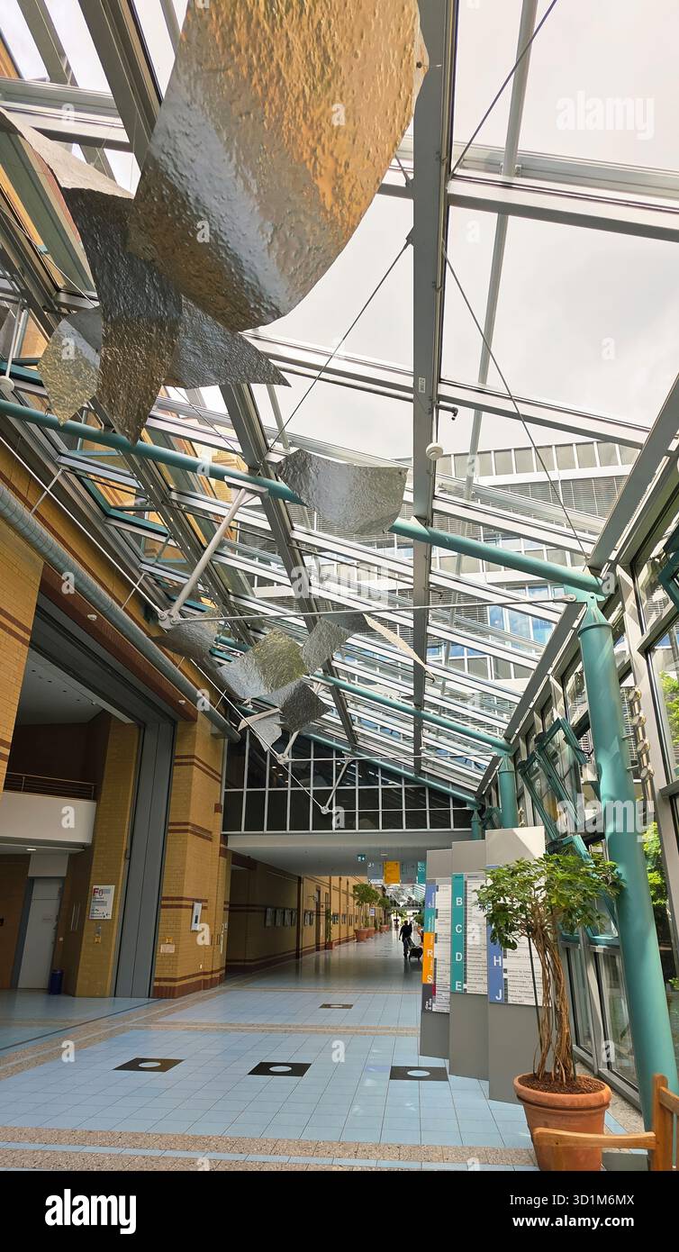 Belin, Germany - May 30, 2025: Modern interior space features a glass roof and artistic metal sculptures hanging above. Hospital - Smartphone Captured Stock Image