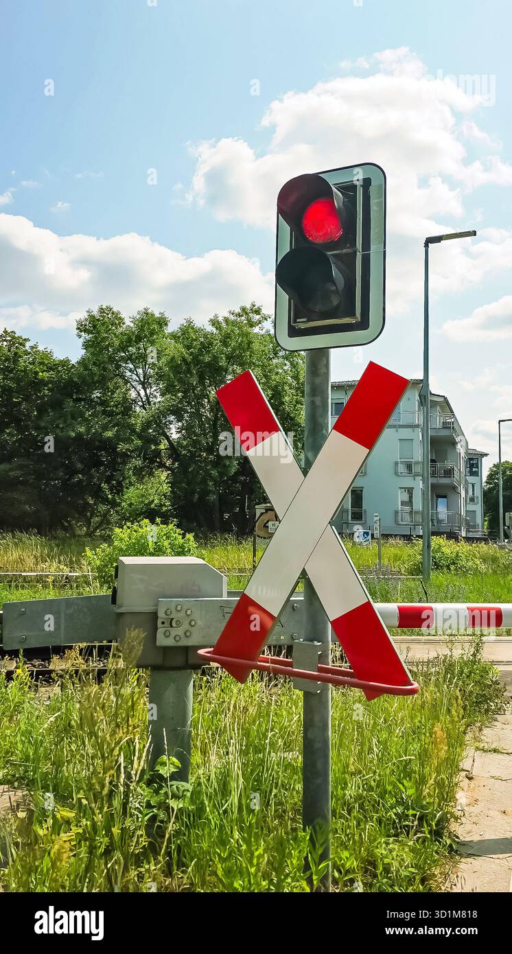 Berlin, Germany - June 11, 2025: Red signal at railway crossing with barrier and lush greenery in the background. - Smartphone Captured Stock Image