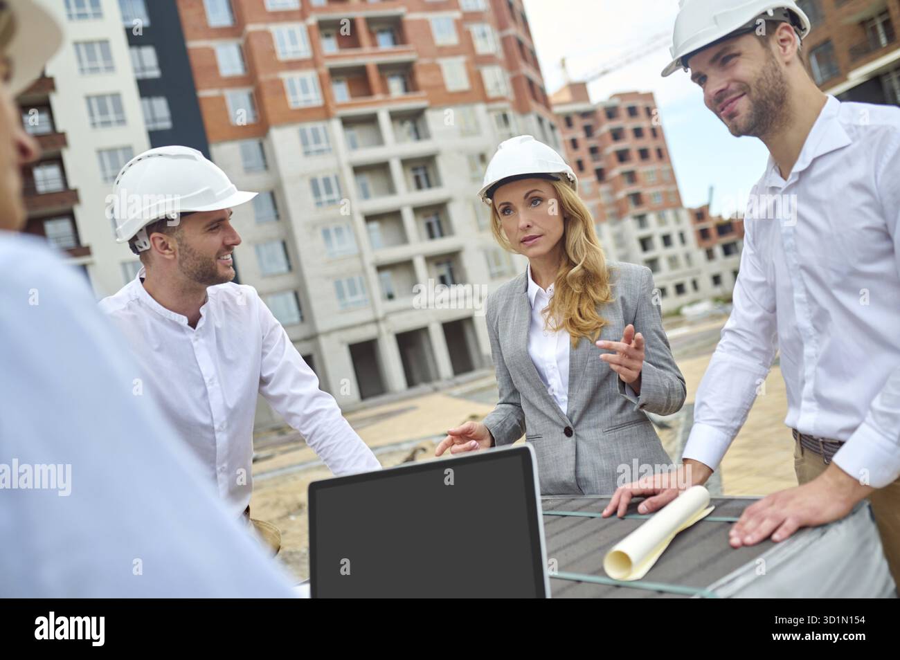 Serious middle-aged female building inspector standing on the construction site surrounded by three male workers Stock Photo