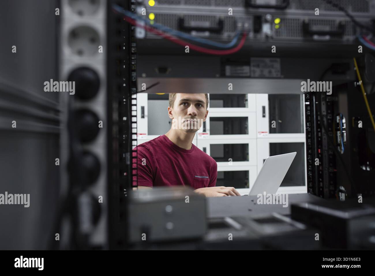 Young man connecting wires in server cabinet while working with supercomputer in data center Stock Photo