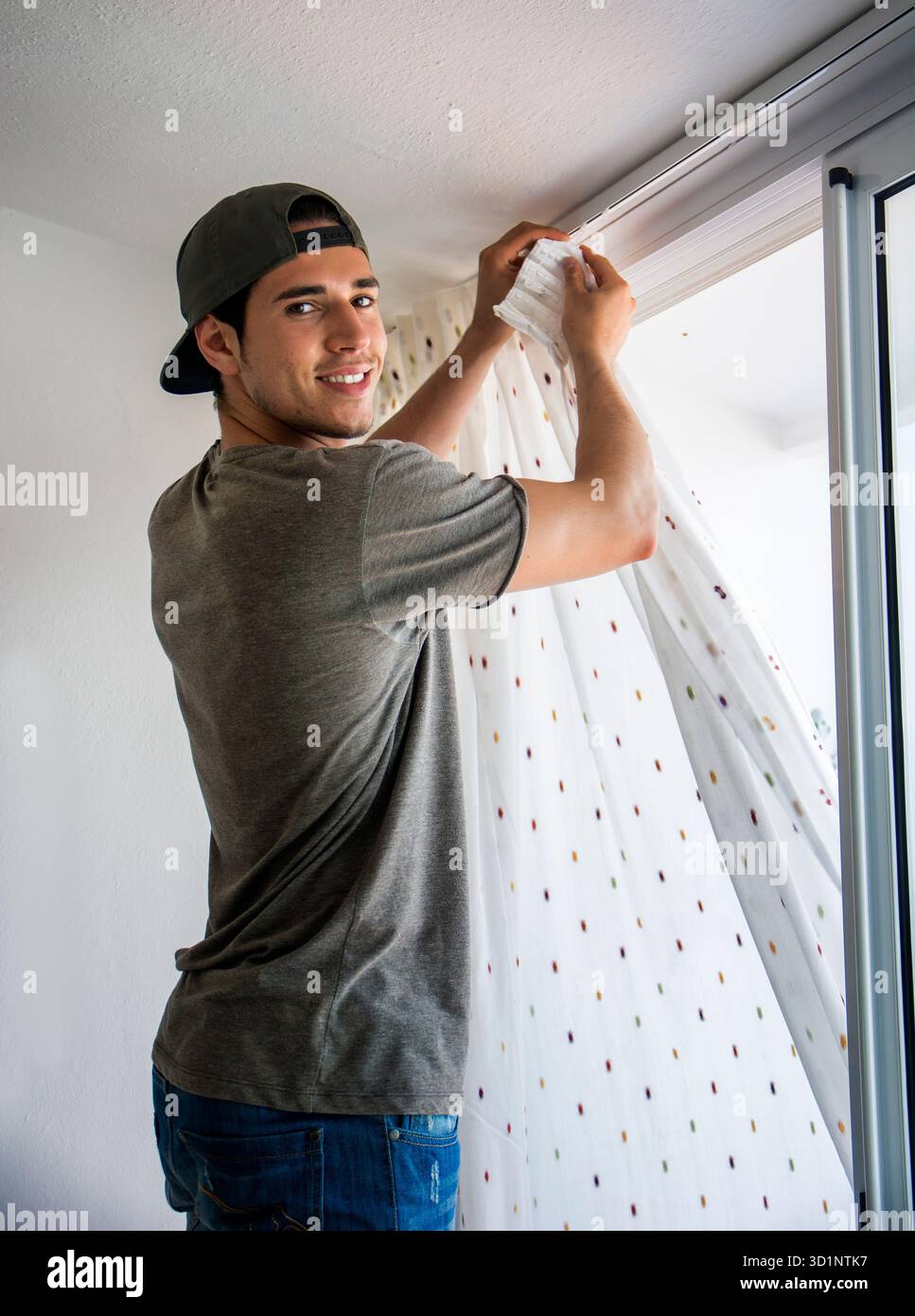 Young man installing curtains over window Stock Photo