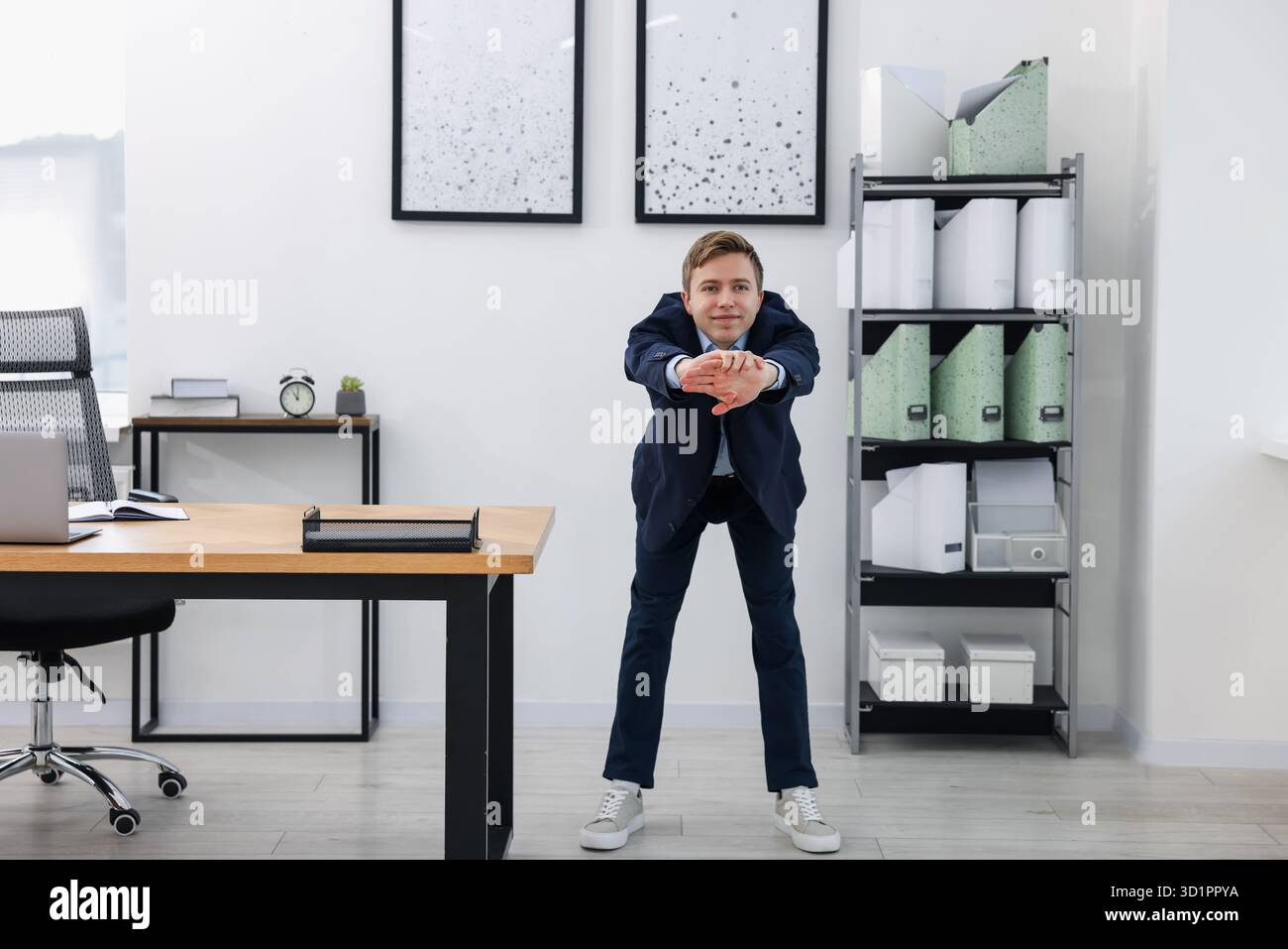 Young businessman doing stretching exercise in office Stock Photo