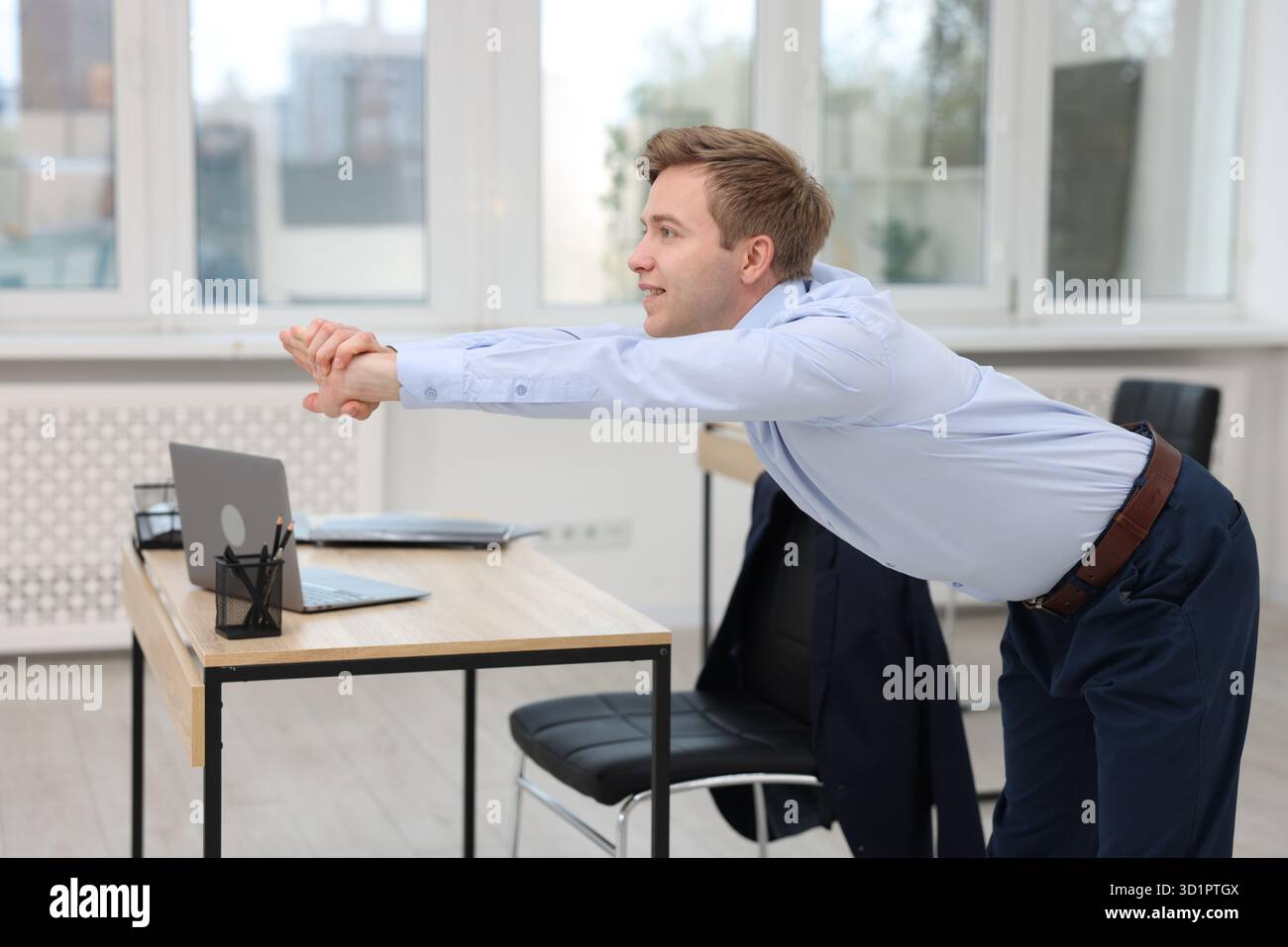 Young businessman doing stretching exercise in office Stock Photo