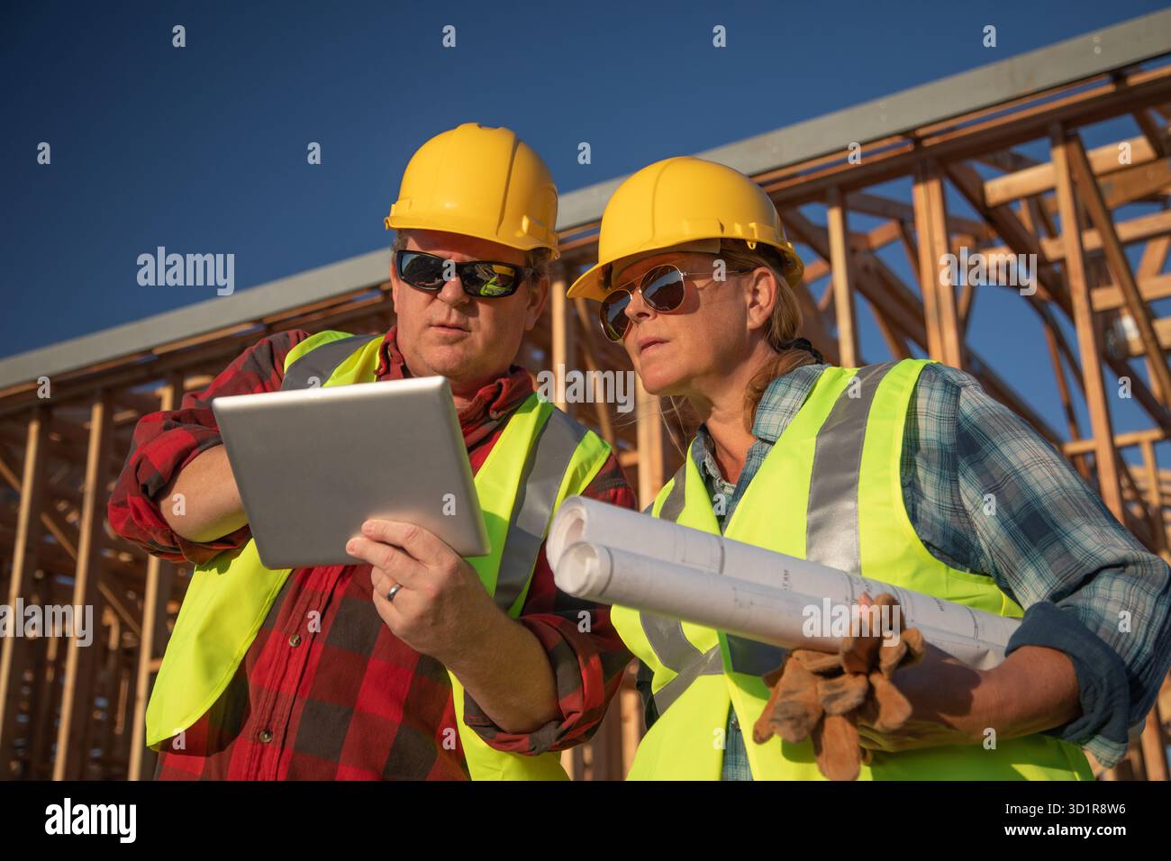 Male and Female Construction Workers Using Computer Pad at Construction Site Stock Photo