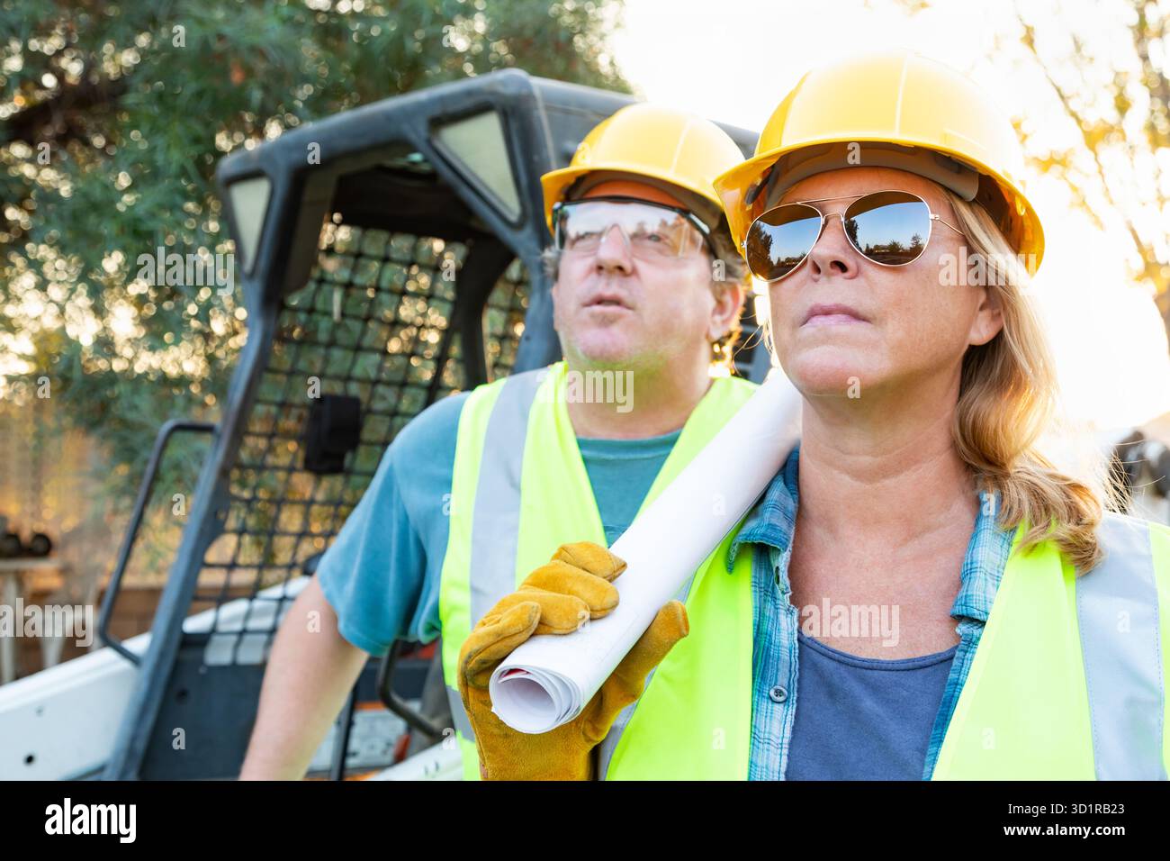 Male and Female Workers With Technical Blueprints at Construction Site Stock Photo