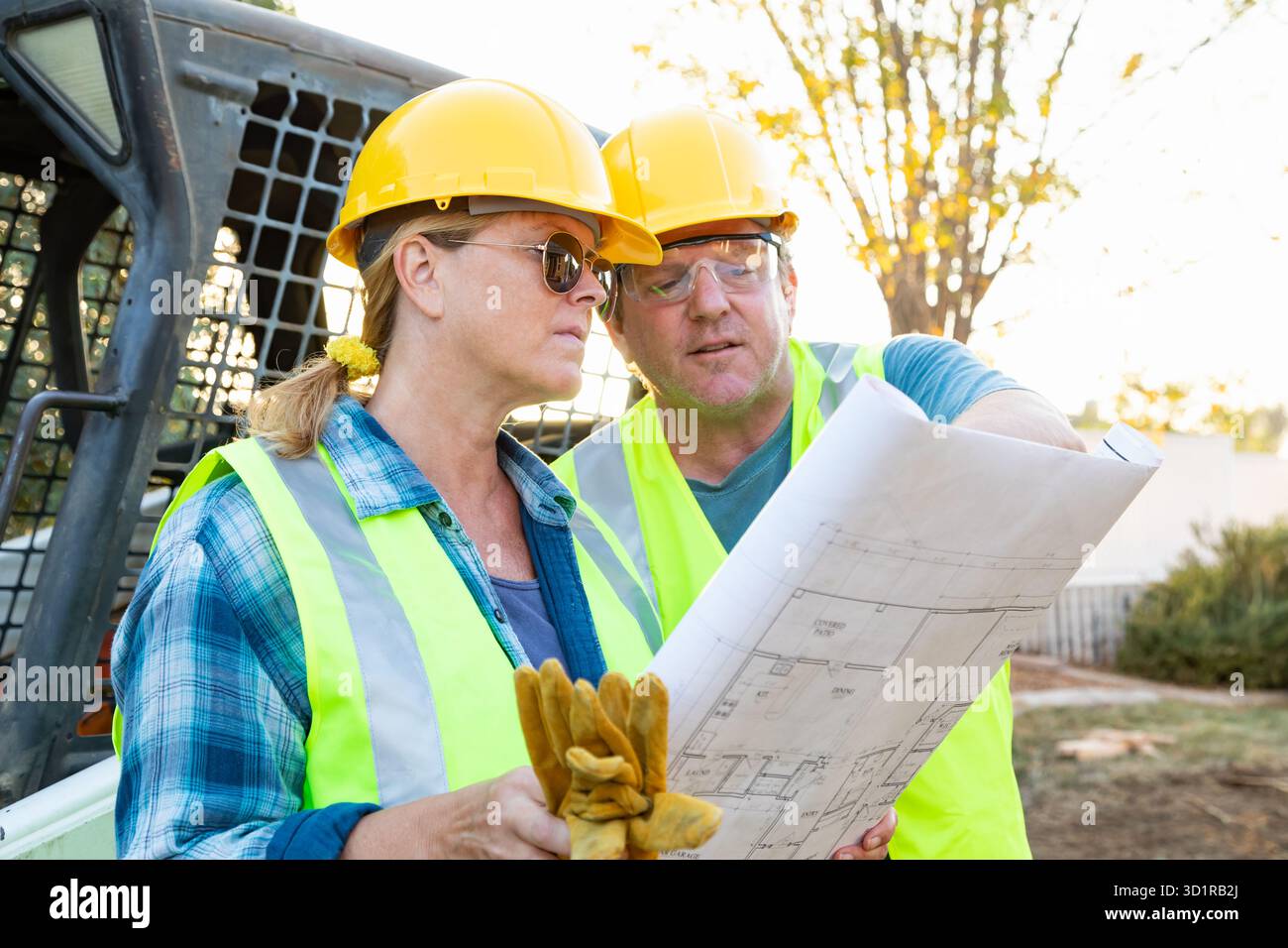 Male and Female Workers With Technical Blueprints Talking at Construction Site Stock Photo