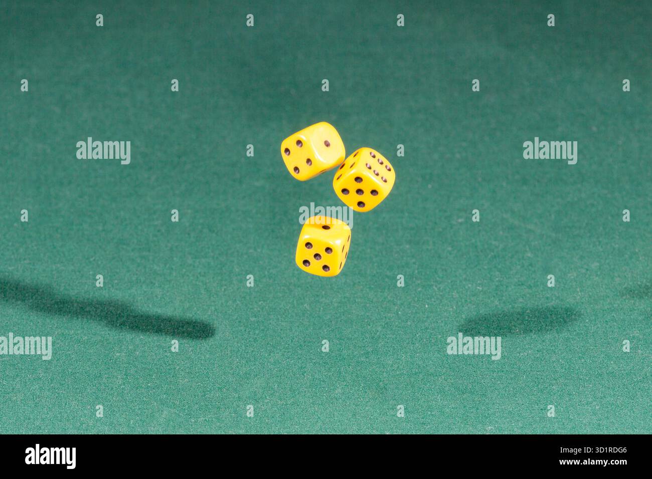 Three yellow dices falling on a green table Stock Photo