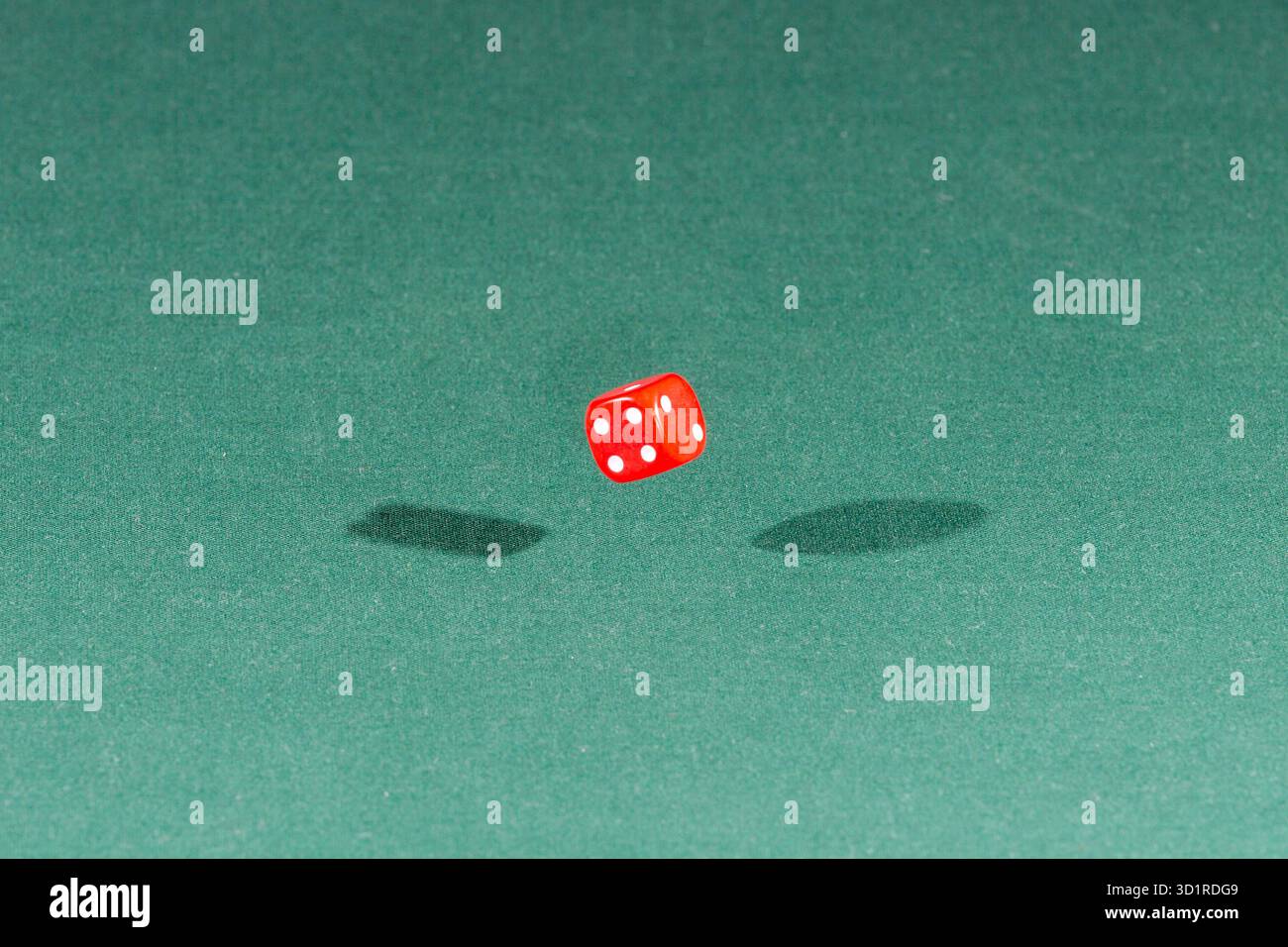 One red dice falling on a green table Stock Photo