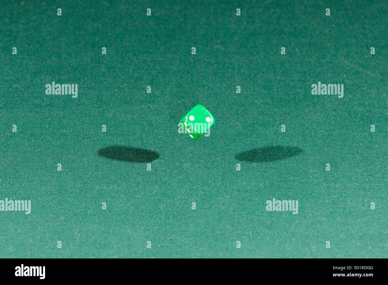 One green dice falling on a green table Stock Photo