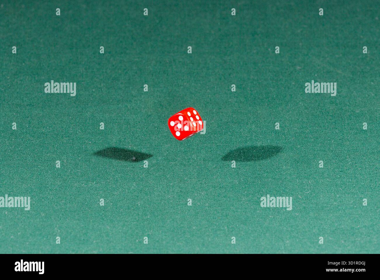 One red dice falling on a green table Stock Photo