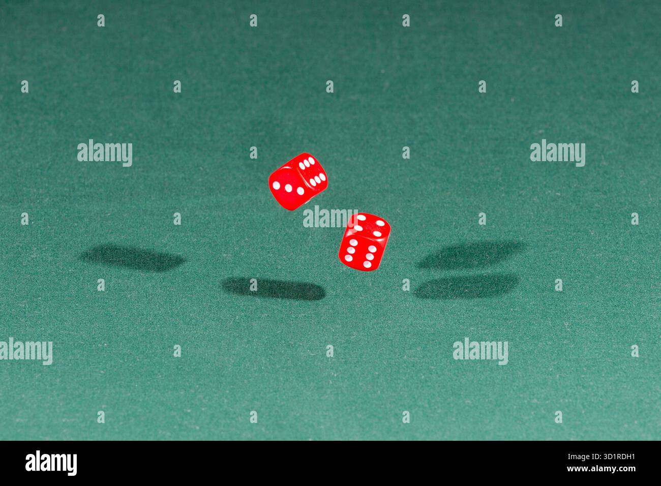 Two red dices falling on a green table Stock Photo