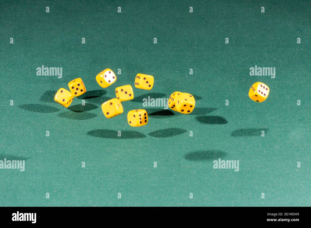 Ten yellow dices falling on a green table Stock Photo