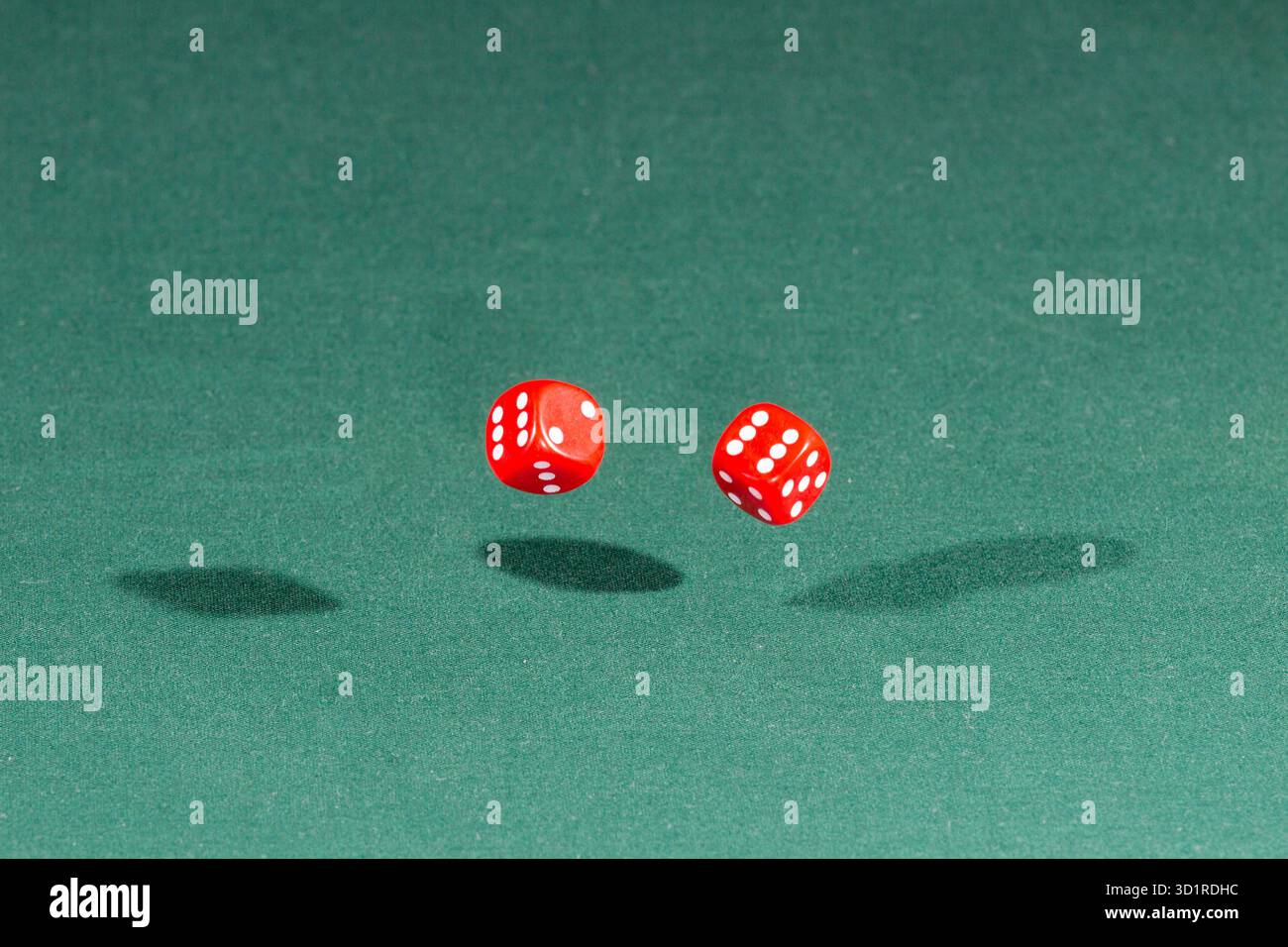 Two red dices falling on a green table Stock Photo