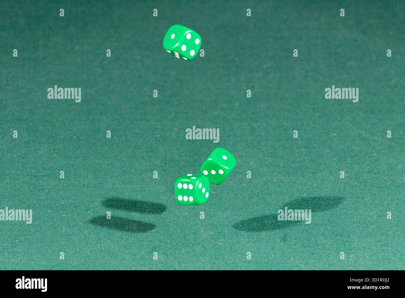 Three green dices falling on a green table Stock Photo