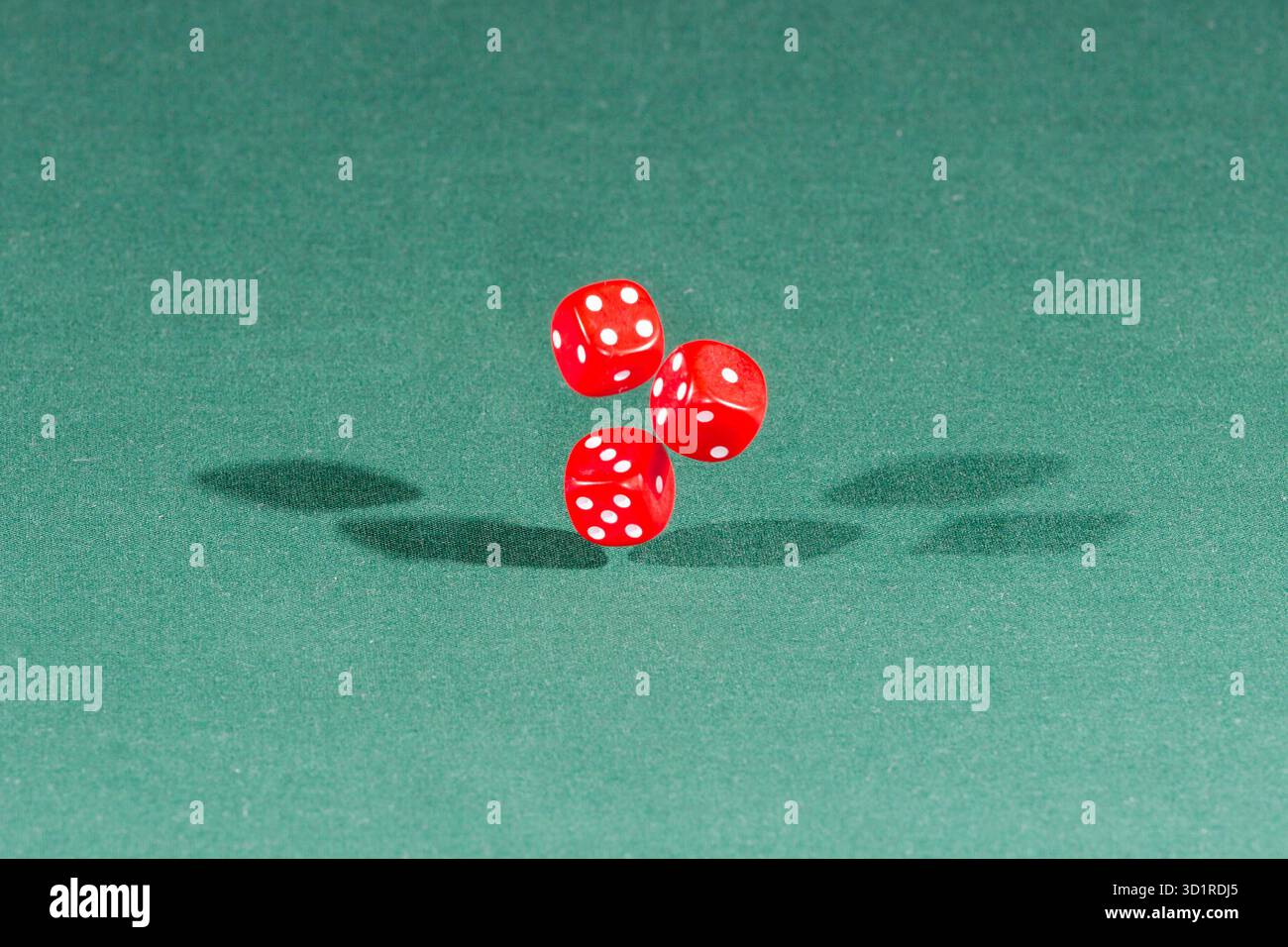 Three red dices falling on a green table Stock Photo