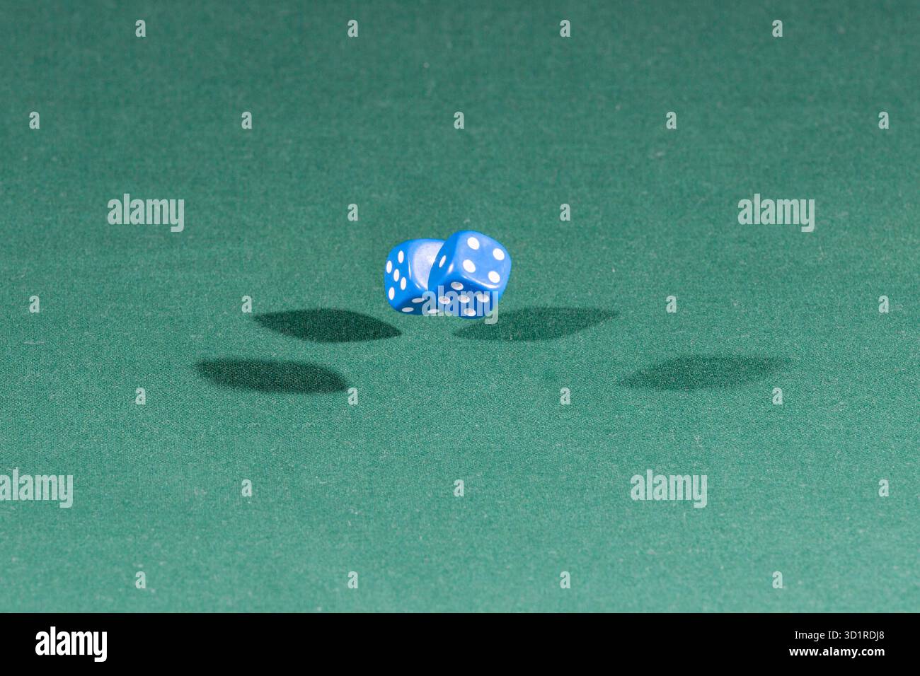 Two blue dices falling on a green table Stock Photo